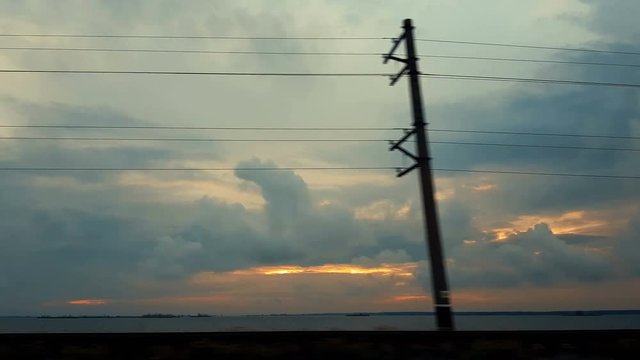 Colorful spring summer landscape on river with beautiful clouds in the sky evening time, shooting from a car that goes on the road along the railway, power lines and water, dynamic scene, 4k video.