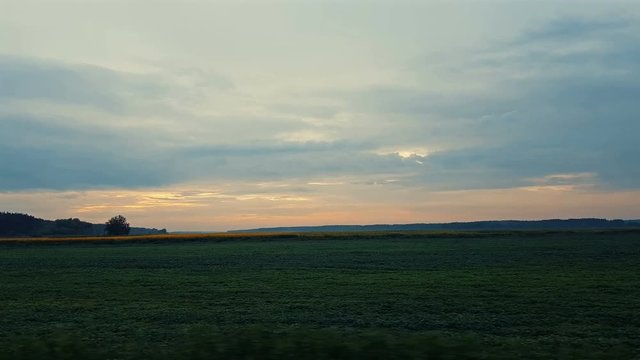 Field and forest in the amazing beautiful clorfull summer sunset. Beautiful thunder clouds over the field, shooting from a car that goes on the road along the ground. Evening, Dynamic scene, 4k video