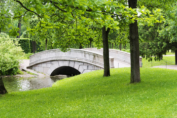Stone bridge with an arch across the stream in the summer Park.