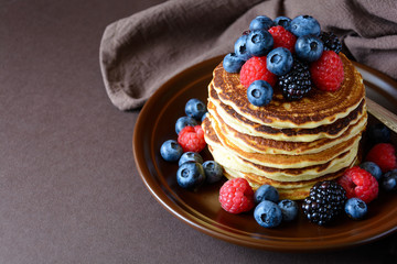 Stack of pancakes with fresh blueberry, raspberry and blackberry on brown plate