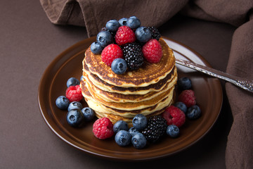 Stack of pancakes with fresh blueberry, raspberry and blackberry on brown plate