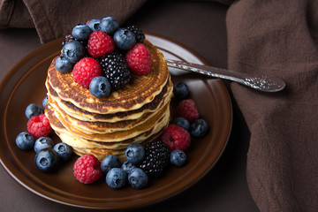 Stack of pancakes with fresh blueberry, raspberry and blackberry on brown plate