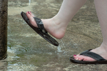 Women's feet in sandals with dark pink toenail polish getting sand washed off after walking on a beach