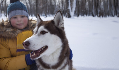 happy boy playing with dog or husky outdoors in winter day.