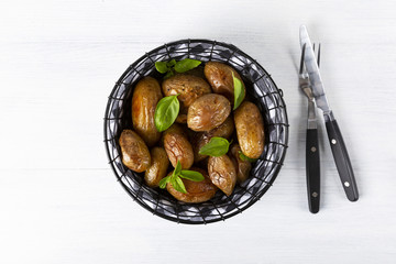 Baked potatoes in a black basket. Knife and fork. The background is white. Copy space. Top view. Horizontal shot.
