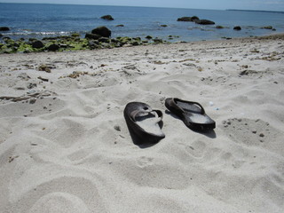 A brown pair of flip flops in the sand at the beach 