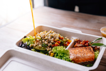 Clean food meal box: Pouring salad dressing over Grilled salmon fillet with tomato and bean sprout salad including carrot and corn.