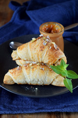 Croissants sprinkled with nuts and sugar powder. A jar of caramel in the background