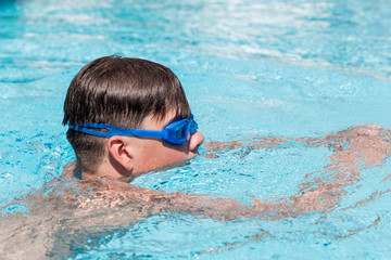 Close-up portrait of teenage boy in goggles in swimming pool.