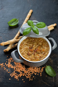 Italian soup with red lentils and pasta in a pot over dark brown stone background, elevated view, vertical shot