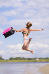 Joyful girl jumps into the sea with a suitcase in a swimsuit.
