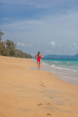 Sexy woman in red swimsuit jumping on the beach near ocean, view from the back, Phuket, Thailand
