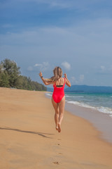 Sexy woman in red swimsuit jumping on the beach near ocean, view from the back, Phuket, Thailand