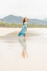 Fashion young lady in long blue dress walk and dance modern choreography in water at beach. Style girl, windy hair, toned, sugaring legs, beach wear, tender skin. Summer day and happy holiday.