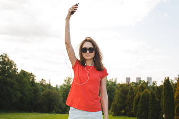 A young girl is having fun walking with a phone in her hands in a summer park.