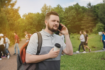 Portrait of a young guy with a beard talking on the phone in a summer park.
