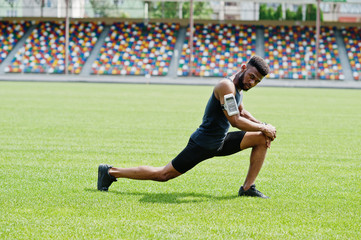 African american male athlete in sportswear doing stretching exercise at stadium.