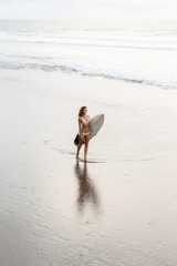Surf girl with long hair go to surfing. Fitness surfer woman holding surfboard on a beach and ready to have fun in ocean water. Bali island, Indonesia. Outdoor Active Lifestyle. It's time for surfing!