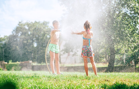 Two kids, brother and sister, play with watering hose in summer garden