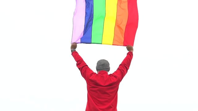 man raise rainbow flag LGBTI flag in hard wind with misty background