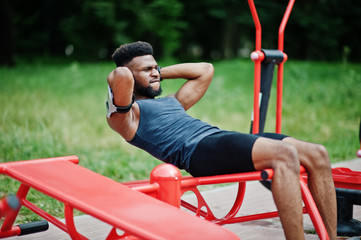 Obraz premium African american male athlete sport man with running sports arm case for mobile phone, doing exercises on the street workout simulators.