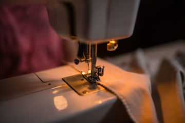 The seamstress sews clothes from the fabric on the sewing machine. Work with the light of the built-in hardware lamp. Steel needle with looper and presser foot close-up