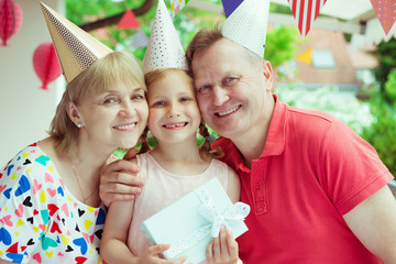 Portrait of happy grandparents celebrating birthday with their pretty little granddaughter on decorated terrace