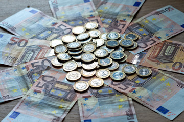 50 euro banknotes and 1 euro coins on a light wood background.