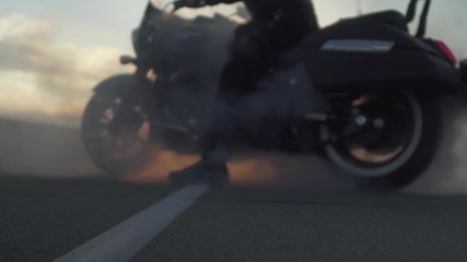 Biker create a smoke with motorcycle at sunset background on road, slow motion