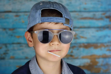 niño con gafas de sol y gorra chupando un caramelo con palo
