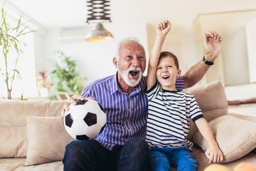 Little boy on couch with grandfather cheering for a football game