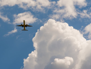 The Plane Flies In The Sky Against The Background Of Clouds

