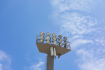 Sports stadium floodlight tower with reflectors with blue sky.