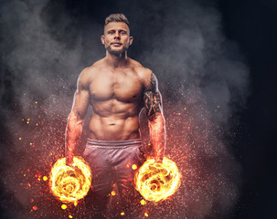 Fototapeta na wymiar Handsome shirtless tattooed bodybuilder with stylish haircut and beard, wearing sports shorts, posing in a studio. Fire art concept.