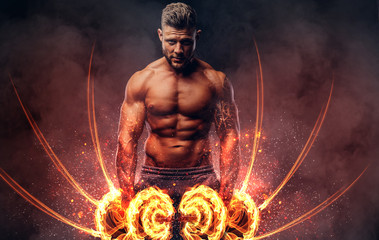 Handsome shirtless tattooed bodybuilder with stylish haircut and beard, wearing sports shorts, posing in a studio. Fire art concept. - obrazy, fototapety, plakaty