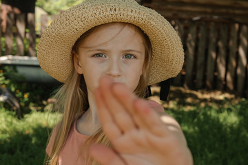 little girl with blonde hair looks evil at the camera and shows her palm in the Park in summer