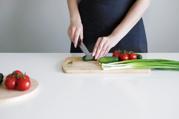 Female hands with a knife, slicing vegetables on a wooden board on a white background.