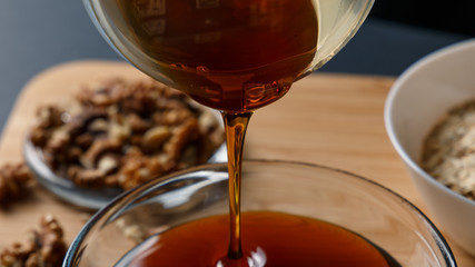 Healthy Breakfast ingredients: honey, walnuts, oatmeal on a dark background. Healthy diet. Close up. Honey pouring