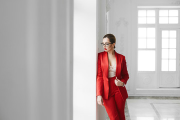 Sexy business lady, plus size model girl in stylish glasses and in red fashionable suit posing near...