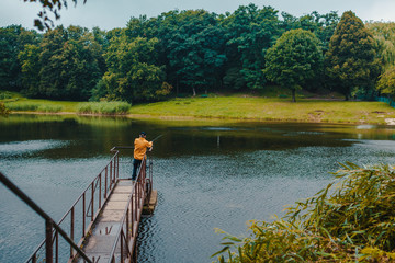 Fisherman standing on pier of the lake and fishing on rainy day