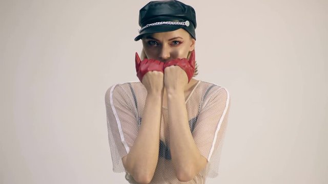 Cat girl concept. A girl wearing a black leather hat covers her face with her hands wearing red leather gloves.