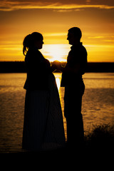 Vertical portrait silhouette of man with his pregnant wife on the beach at yellow sunset