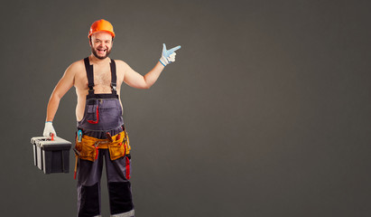 Funny fat bearded builder with a tool box points to a gray background for text.