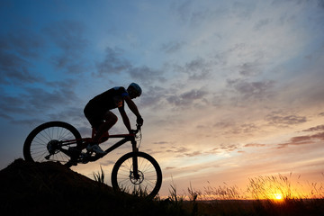 Silhouette of a bicyclist wearing a helmet and sportswear on a mountain bike coming down the hill...