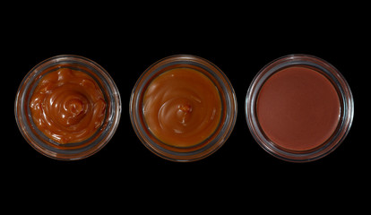 Top view of pots with caramel, cocoa butter and chocolate oil isolated on black