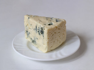 Gorgonzola cheese with blue mold on white plate on light background