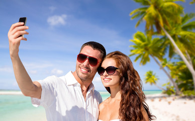 travel, tourism and summer vacation concept - smiling couple in sunglasses making selfie by smartphone over tropical beach background in french polynesia