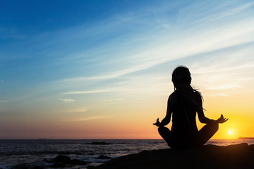 Yoga woman Silhouette doing exercises on the sea beach during sunset.