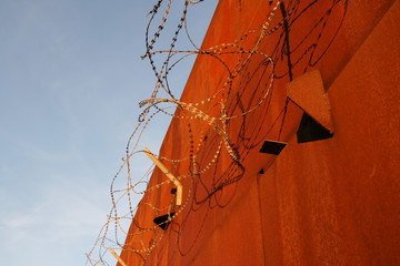 Rote Mauer mit Stacheldraht vor blauem Himmel