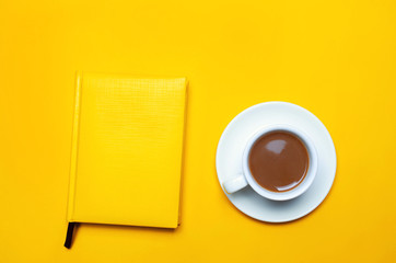 a cup of coffee and notebook. with a saucer and female hands with a yellow manicure on a yellow background. minimalism. place for text. copy space. top view. flat lay